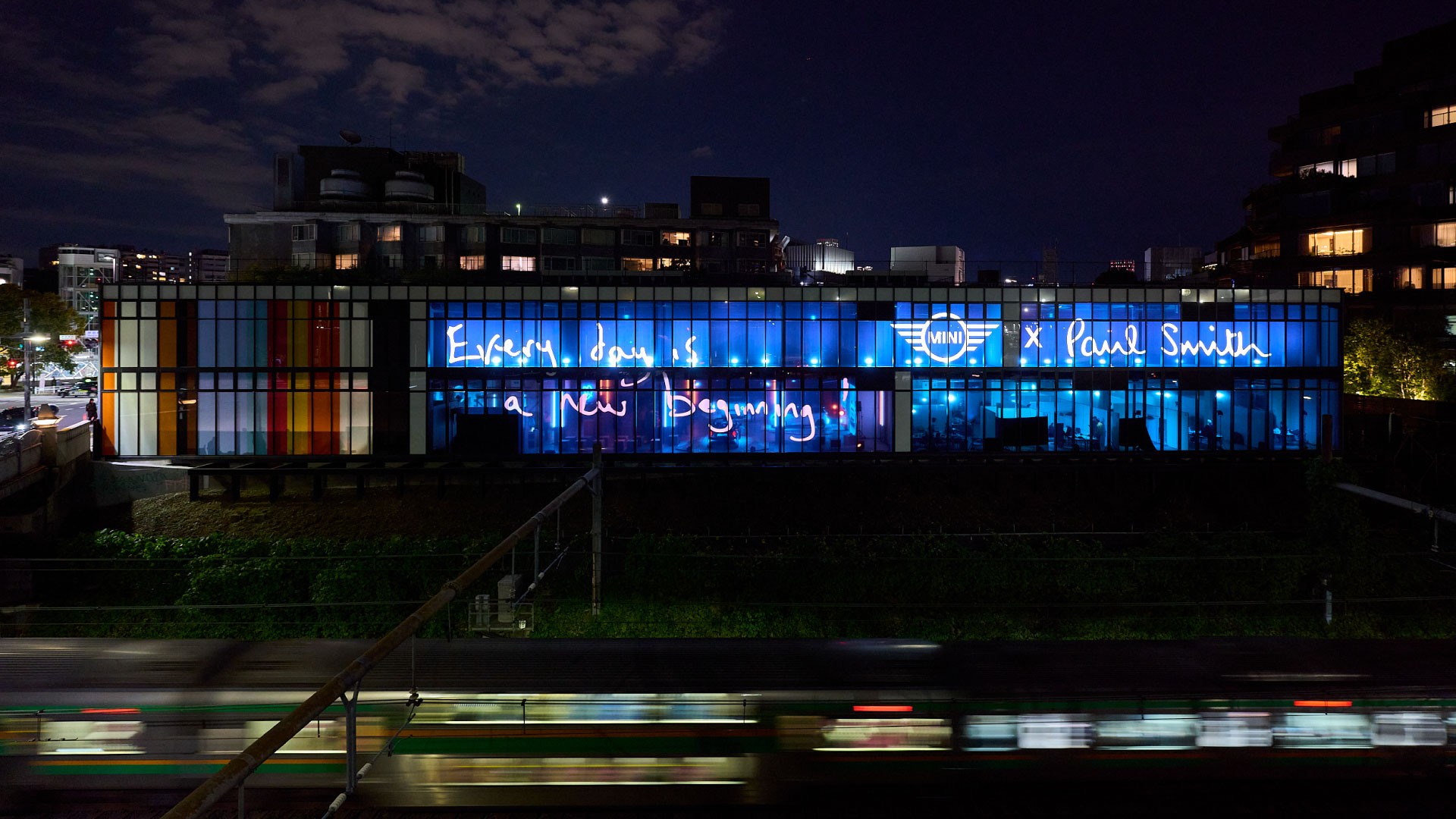 In the darkness of night, the MINI and PAUL SMITH logos appear illuminated on the windows, bathed in the light from the event venue